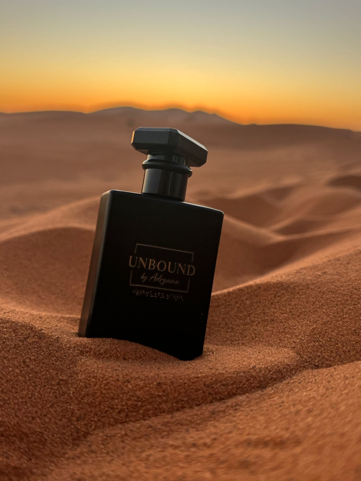 Frasco UNBOUND sobre dunas ao pôr do sol